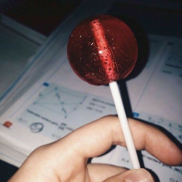 a hand holding a red lollipop on top of a table