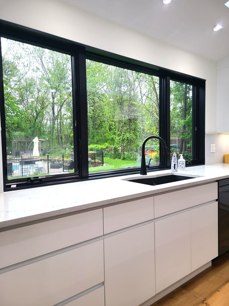 a kitchen with white cabinets and black windows