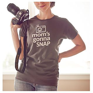 a woman holding a camera in her right hand and wearing a t - shirt that says mom's gomma snap