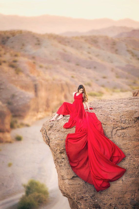 a woman in a red dress is sitting on a rock