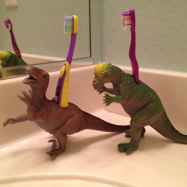 two toy dinosaurs playing with toothbrushes in a bathroom sink