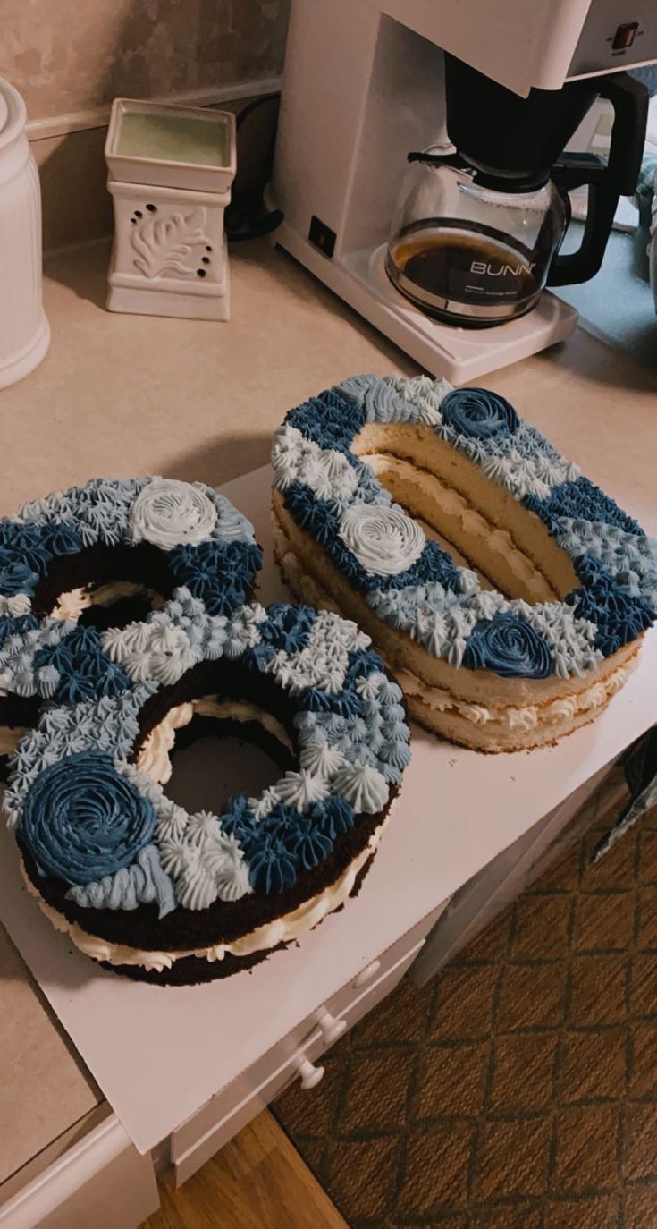 two blue and white frosted cakes sitting on top of a counter next to a coffee maker