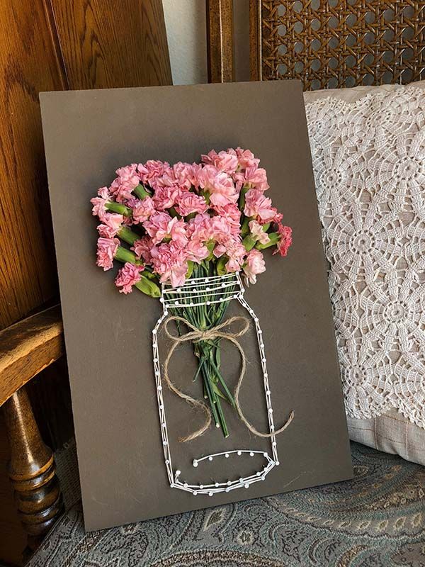 pink flowers are in a mason jar on a gray card with white string tied around it