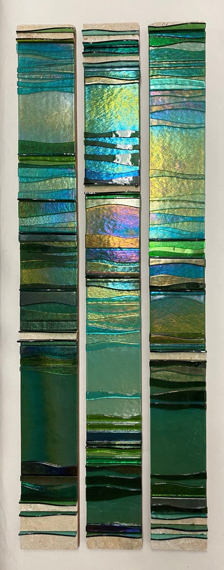 three pieces of stained glass sitting on top of a white wall