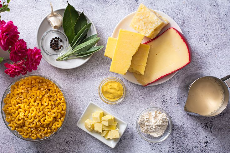 several different types of cheeses and other food items on a white table with flowers