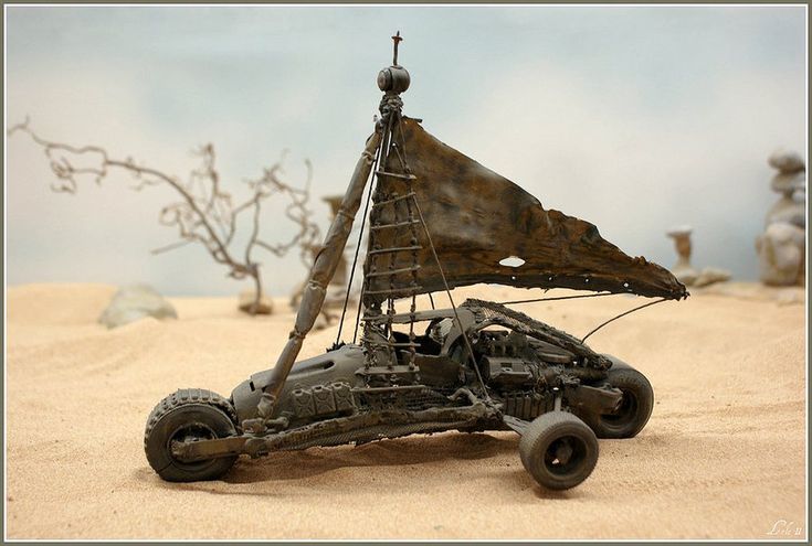 a toy car that is sitting in the sand with a sailboat on it's roof