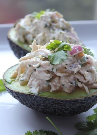 an avocado filled with tuna salad on top of green garnish and cilantro