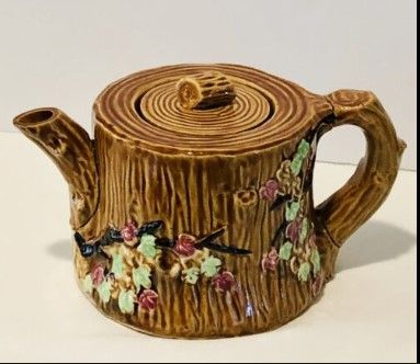 a ceramic teapot decorated with flowers and vines on it's side, sitting on a white surface