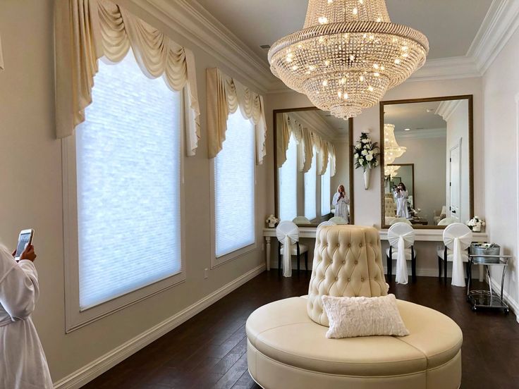 a woman taking a photo of a room with a round couch and chandelier