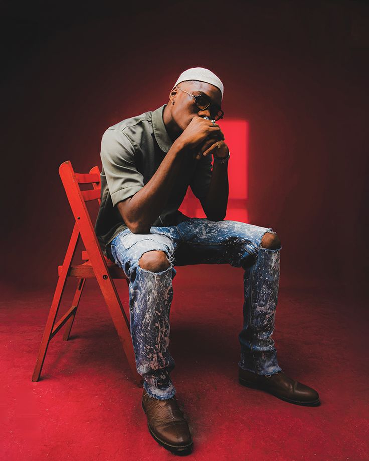 a man sitting in a red chair with his hand on his chin and looking at the camera