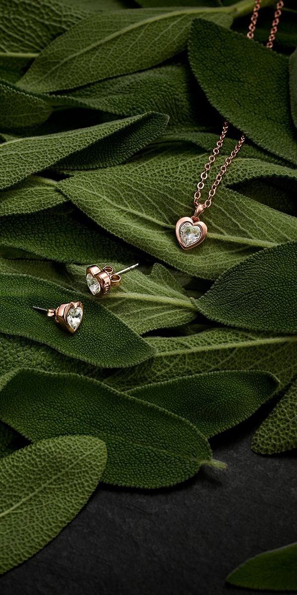 two gold heart pendants sitting on top of green leaves