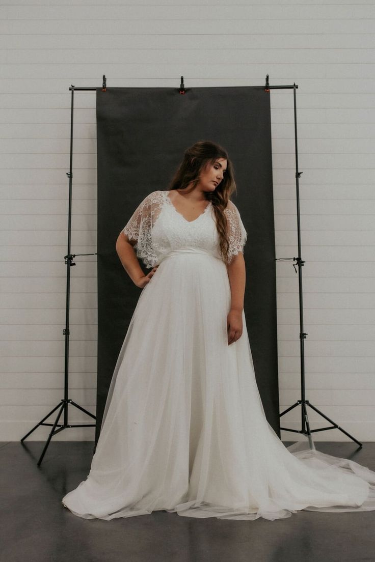 a woman standing in front of a black backdrop wearing a white dress and holding her hands on her hips