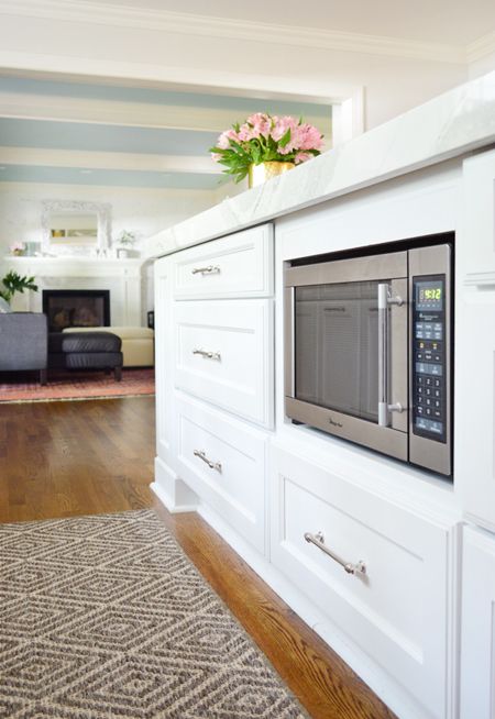 a kitchen with white cabinets and stainless steel microwave on the wall, along with a floral centerpiece