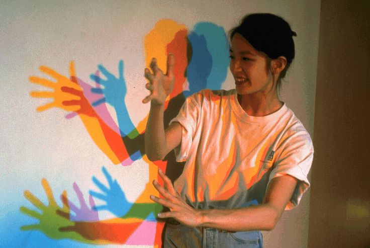 a woman is standing in front of a wall with hand prints on it and holding her hands out