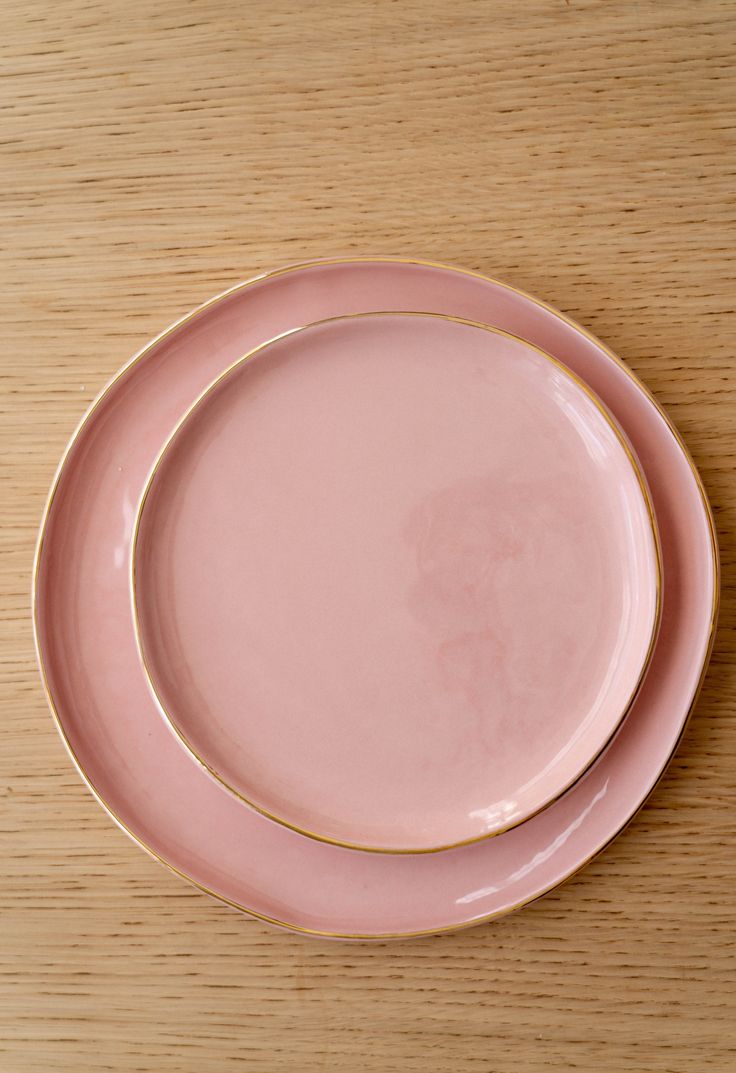 two pink plates sitting on top of a wooden table next to each other with gold rims