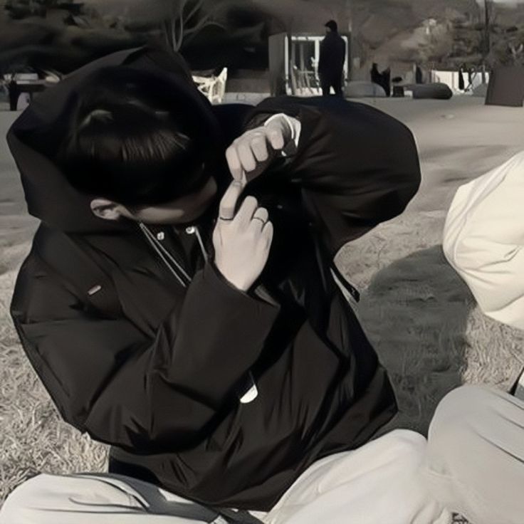 two young men sitting on the ground with their backs to each other, one is covering his face