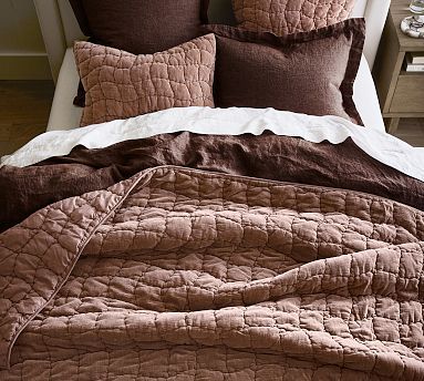 a bed with brown and white comforters on top of it next to a night stand