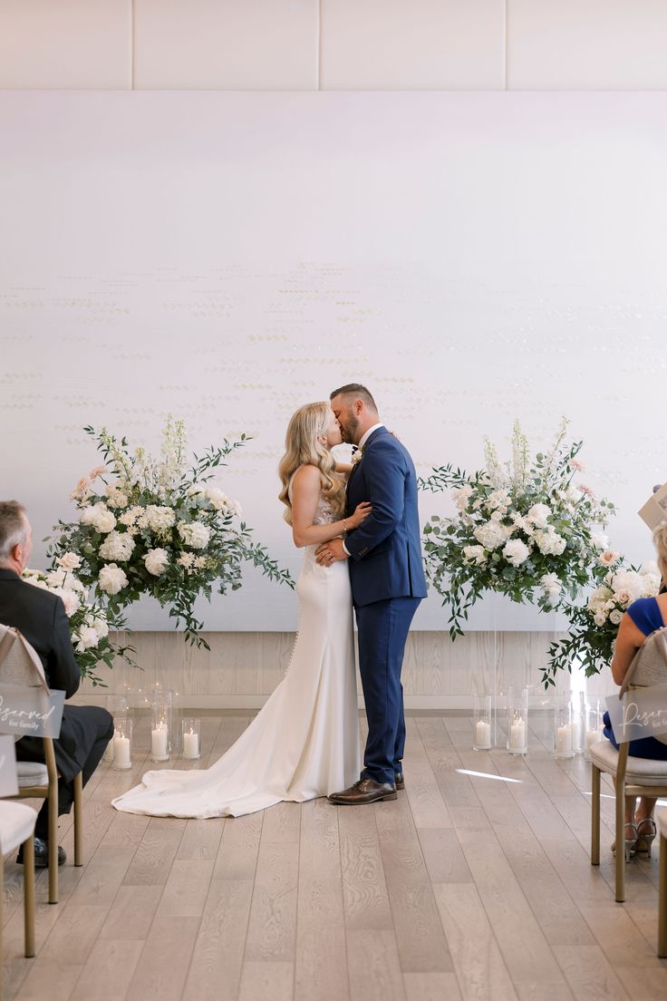 a bride and groom kissing in front of an aisle with flowers on the wall behind them