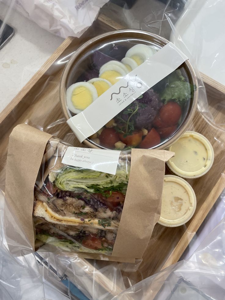 a sandwich in a plastic wrapper with eggs on top and other food items around it