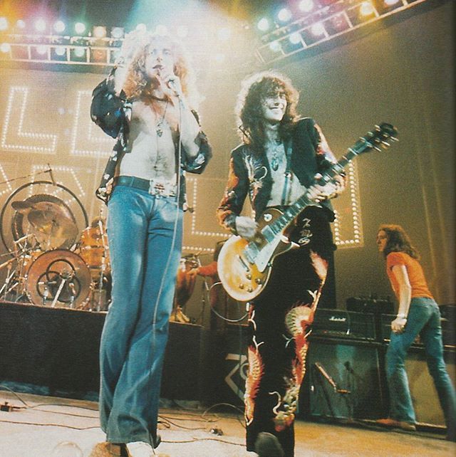 two people standing on stage with guitars in their hands and one person holding an electric guitar