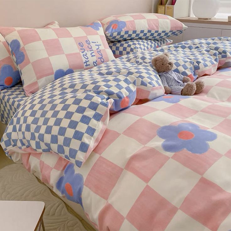 a teddy bear sitting on top of a pink and blue checkered bed