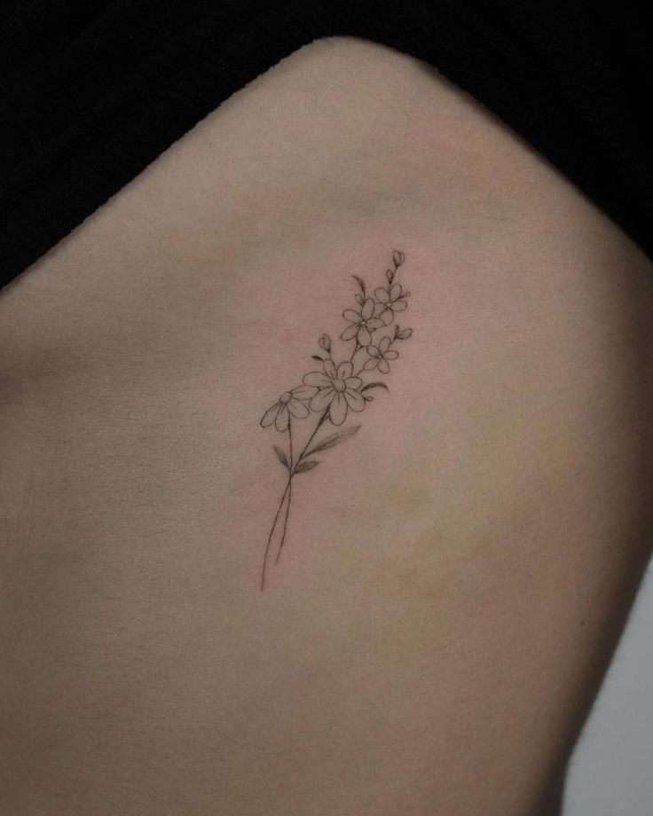 a small flower tattoo on the back of a woman's left side ribcage