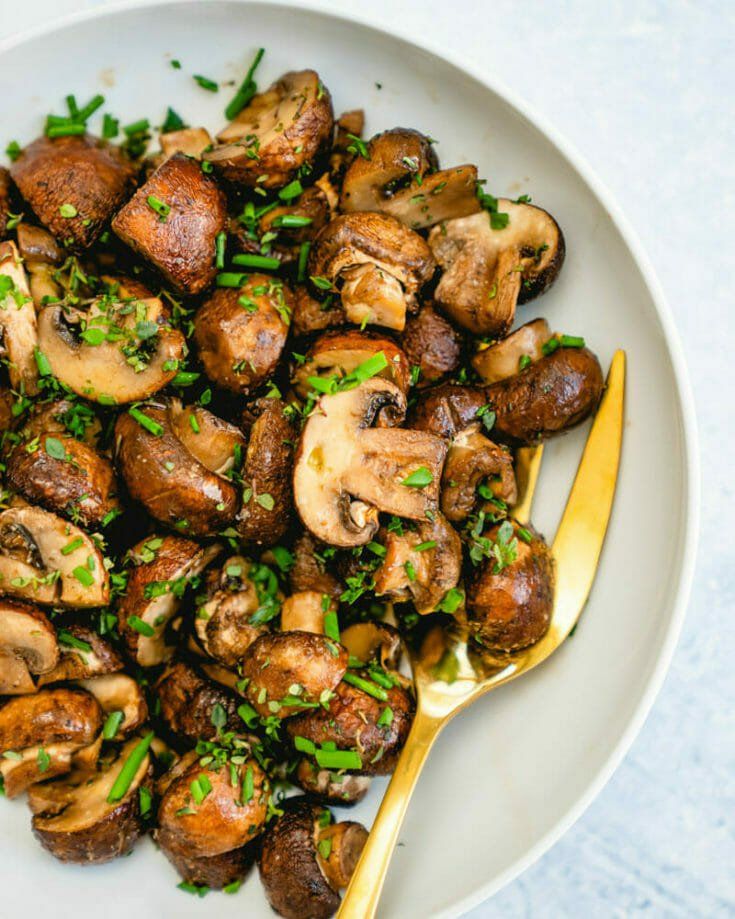 a white plate topped with mushrooms covered in parsley next to a gold spoon and fork