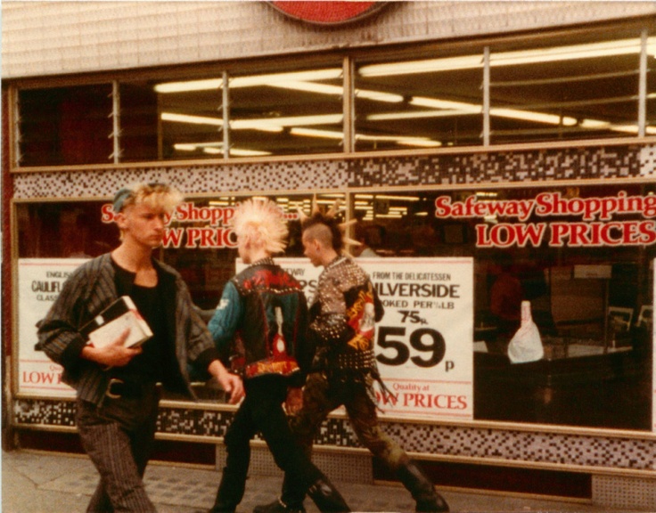 three people walking down the sidewalk in front of a store with signs on the windows