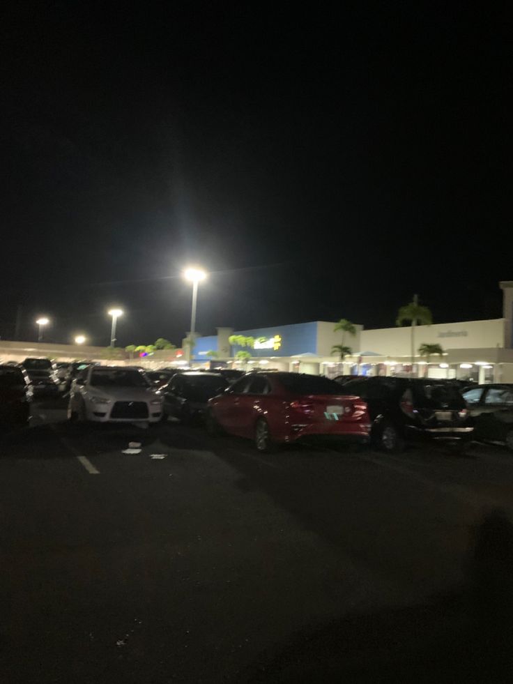 a parking lot filled with lots of parked cars at night in front of a store