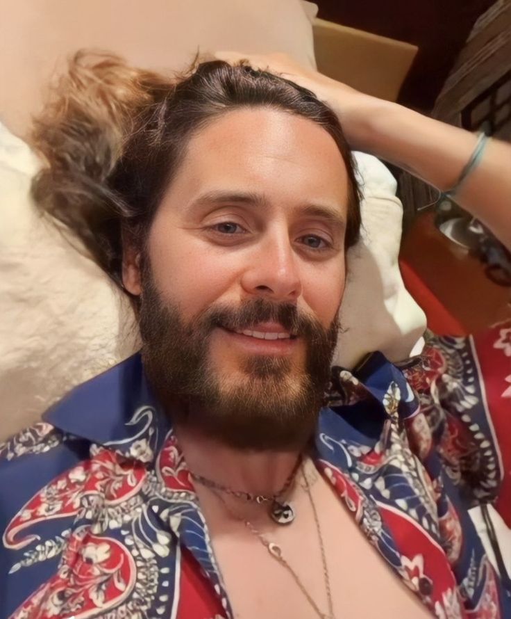 a man with long hair and beard wearing a red, blue and white patterned shirt