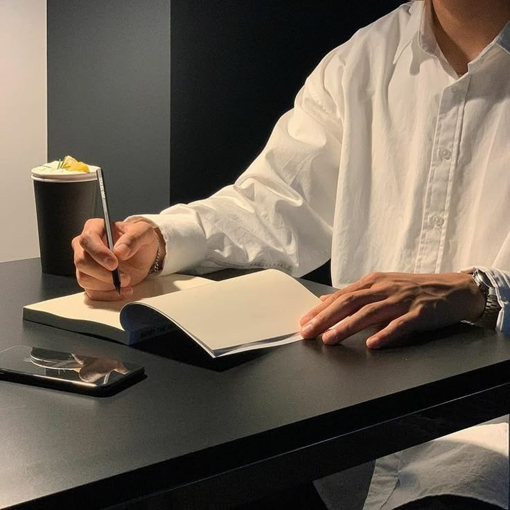 a man sitting at a desk writing on a notepad and holding a pen in his hand