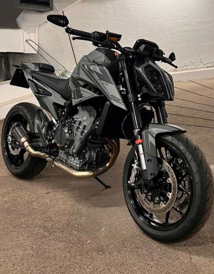 a black motorcycle parked in front of a white wall and some stairs on the ground