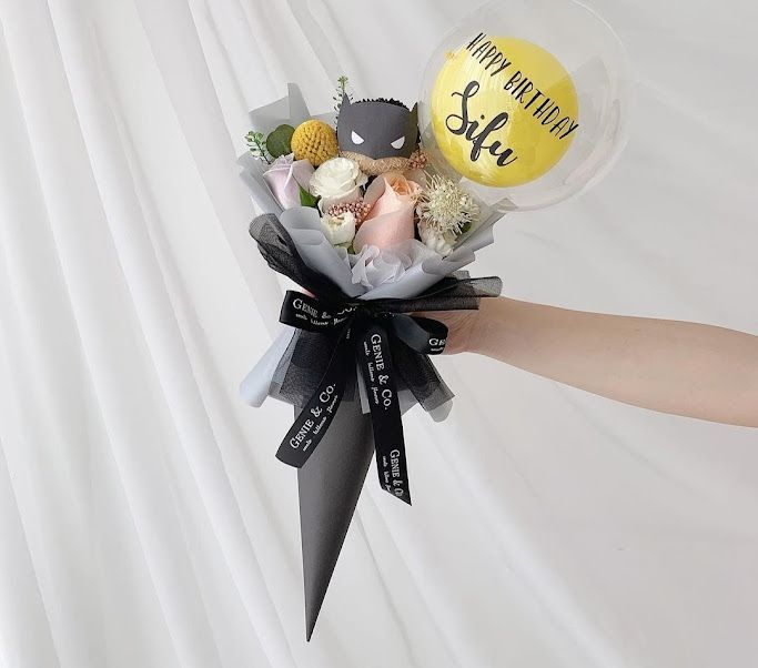 a person's hand holding a bunch of flowers and balloons