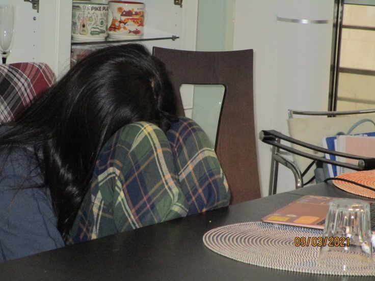 a woman sitting at a table with her head on the back of a chair looking down