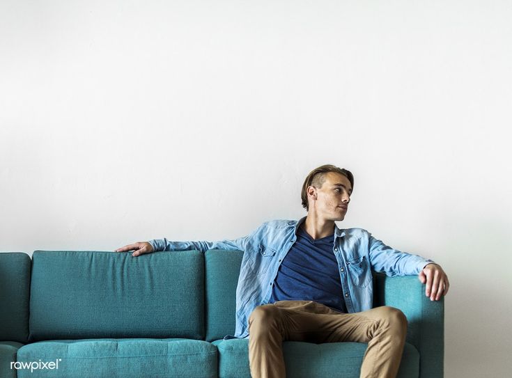 a man sitting on top of a blue couch in front of a white wall with his arms crossed