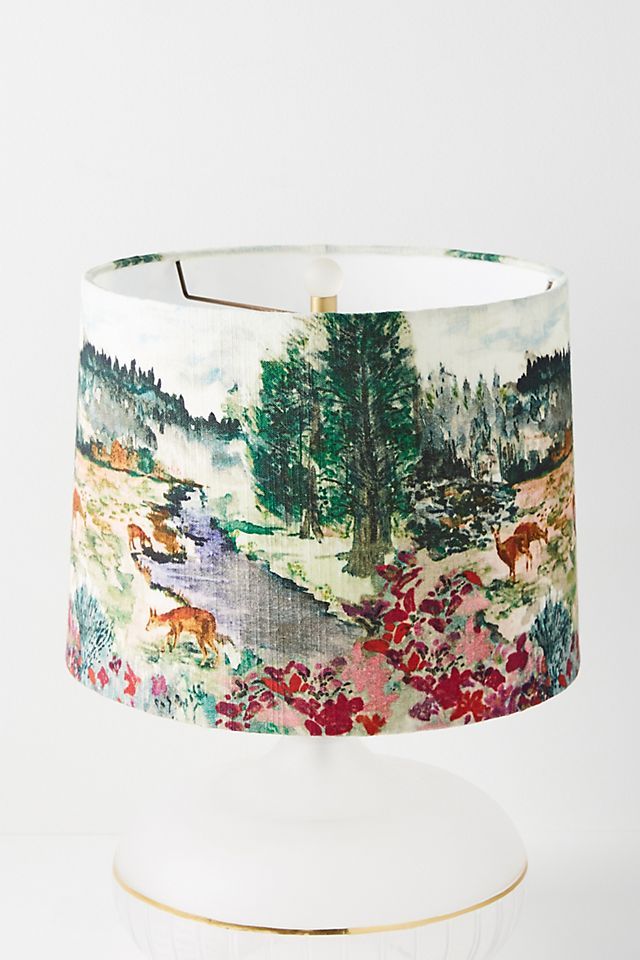 a lamp shade that is on top of a white plate with flowers and trees in the background