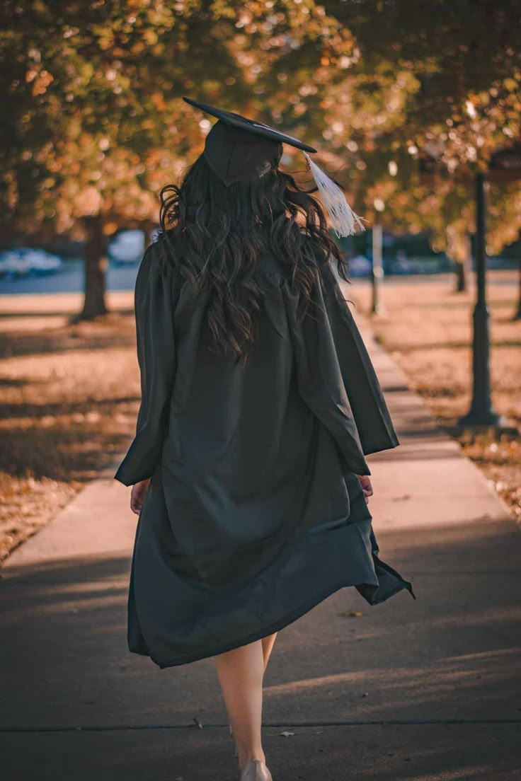 a woman in graduation gown walking down the street with her hat on and long hair