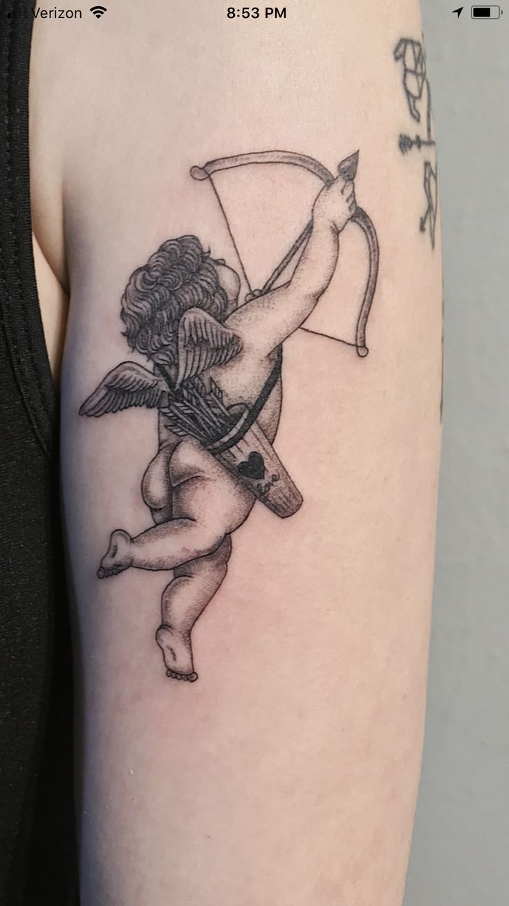 an arrow and cupid tattoo on the left upper half of the arm is shown