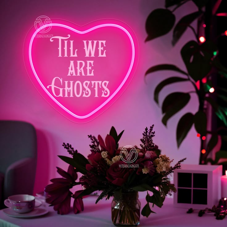 a pink neon sign that says til we are ghost's with flowers in a vase