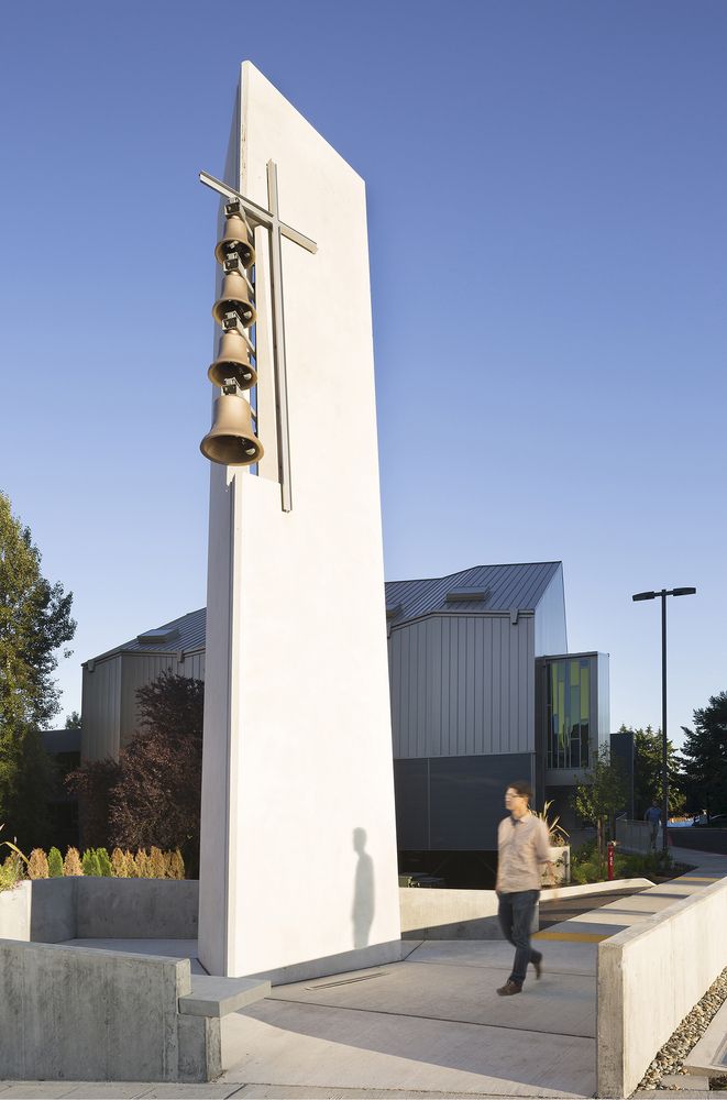 a woman walking past a tall white monument with bells hanging from it's side