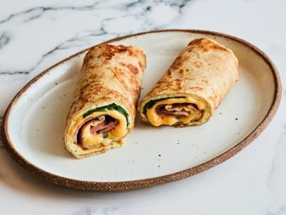 two burritos on a plate with cheese and spinach