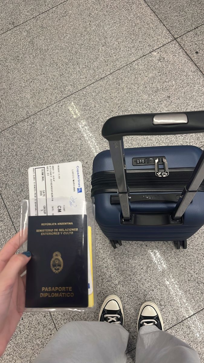 a person is holding a passport and standing next to their luggage