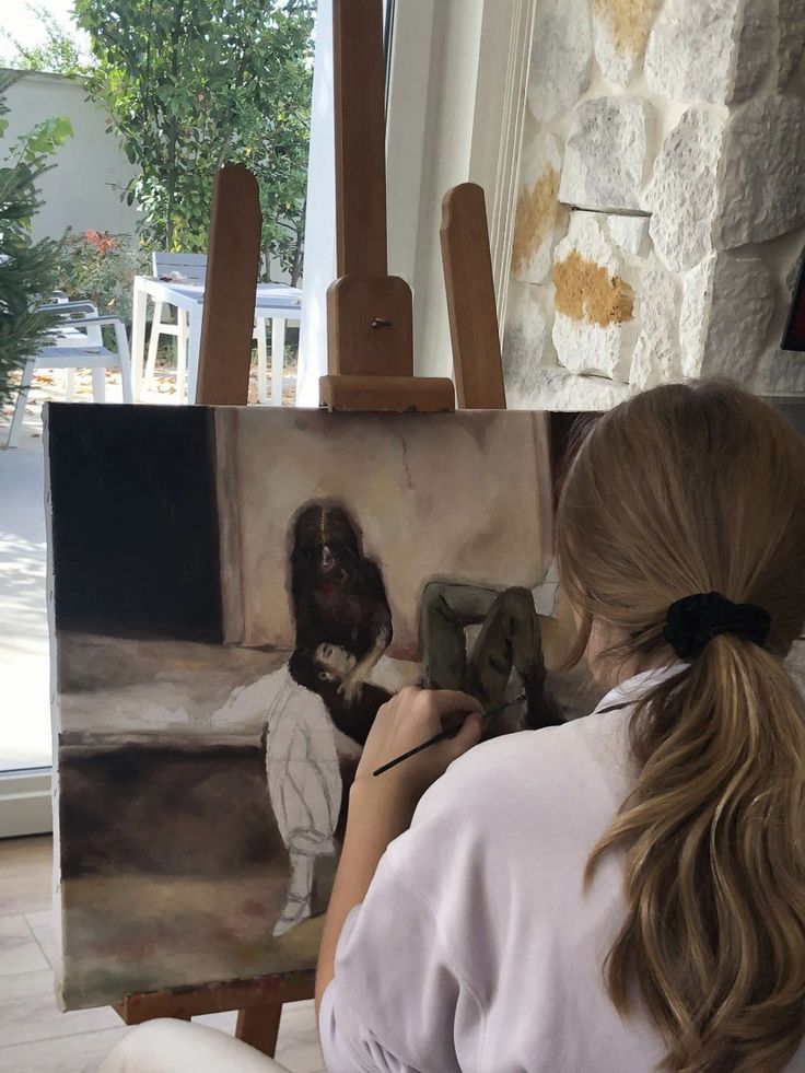 a woman sitting in front of an easel with a painting on it's side