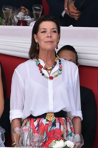 a woman sitting at a table wearing a white shirt and multicolored flower skirt