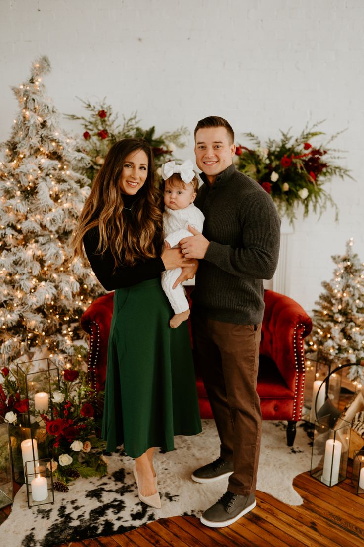 a man and woman holding a baby in front of a christmas tree