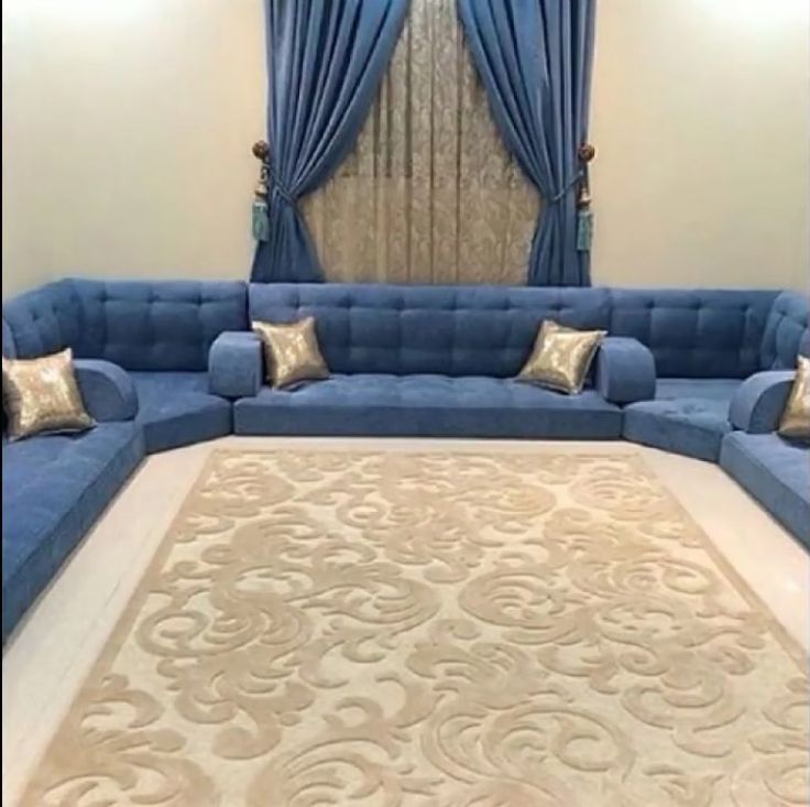 a living room with blue couches and gold pillows on the rug in front of it