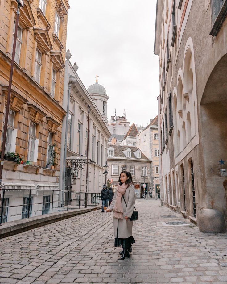 a woman standing in the middle of an alley way with buildings on both sides and cobblestone streets