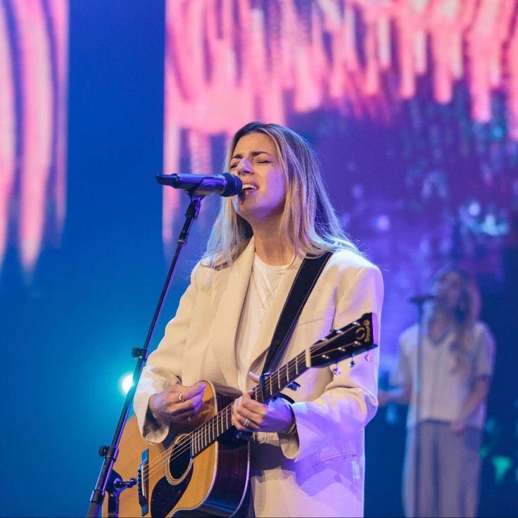 a woman singing into a microphone while holding a guitar