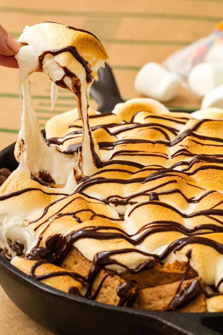 a person is dipping marshmallows into a skillet with chocolate sauce on top