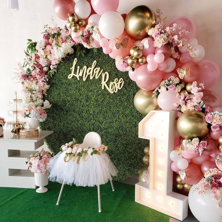 a birthday party with balloons and flowers on the wall, decorated in pink, gold and white